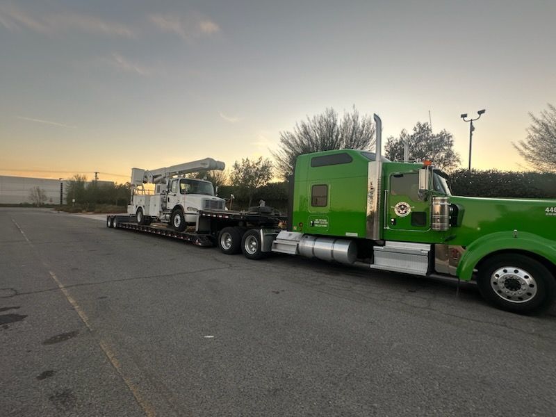 Utility service truck loaded on a lowboy trailer at sunset