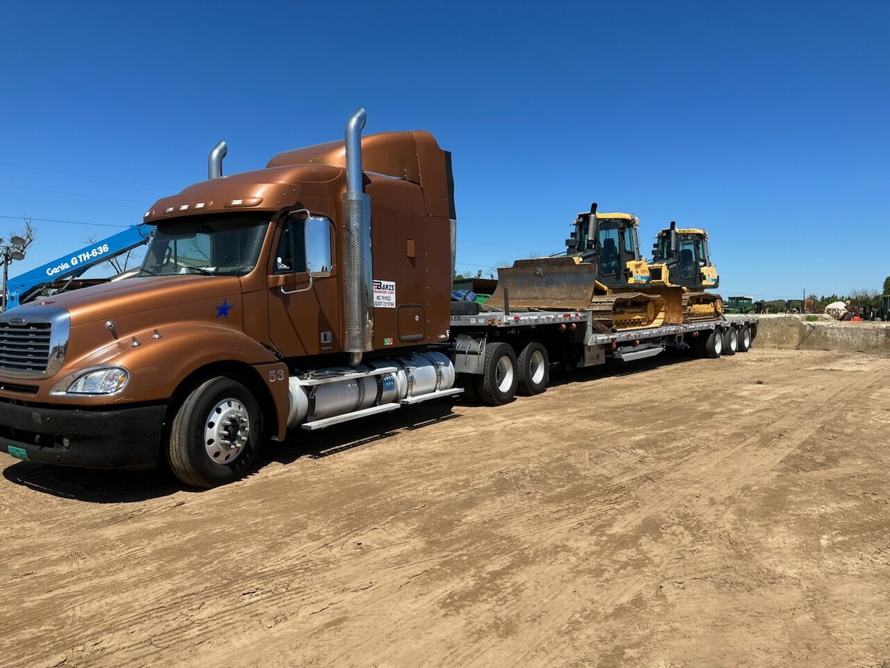 Two dozers loaded on a step deck trailer behind a Freightliner