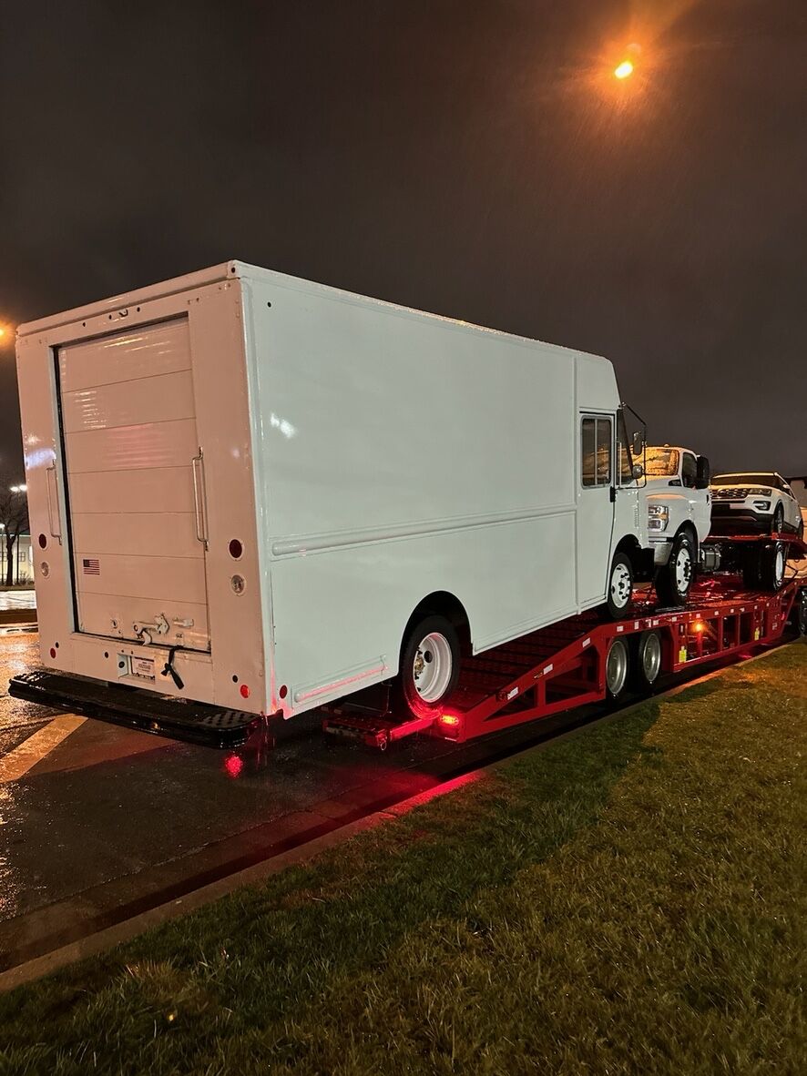 Box truck and pickup loaded on a car hauler trailer at night